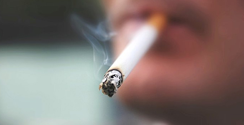 Close up a rostro masculino con cigarro encendido en boca.