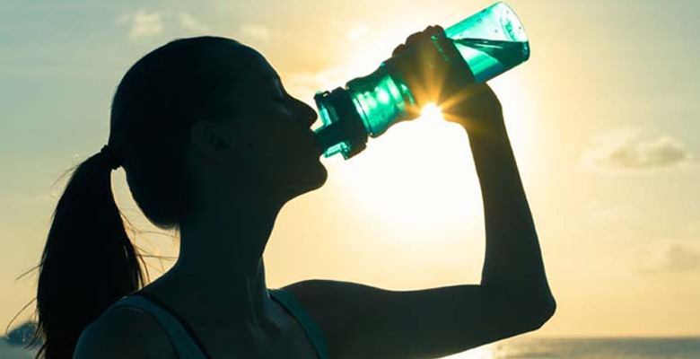 Mujer a contraluz bebiendo agua de una botella.