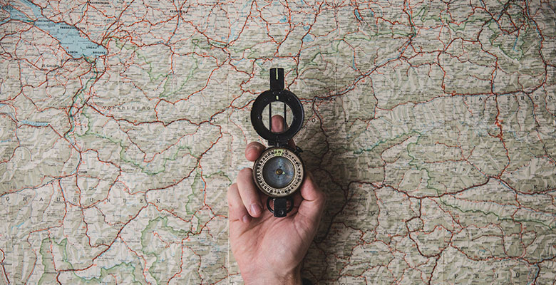 Detalle de una mano sosteniendo una brújula sobre un mapa. 