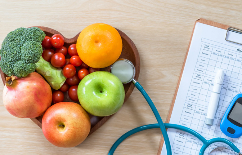 Toma en picada de un escritorio con bowl con frutas y vegetales, y una hoja de registro médico, un estetoscopio y lector de insulina.