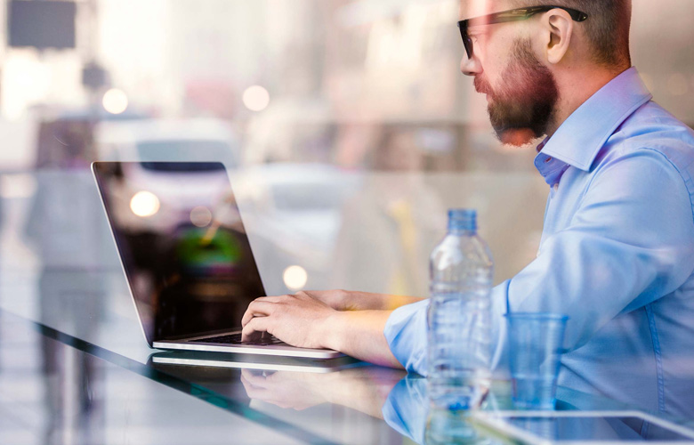 Hombre trabajando con laptop en escritorio con una botella de agua a un lado.