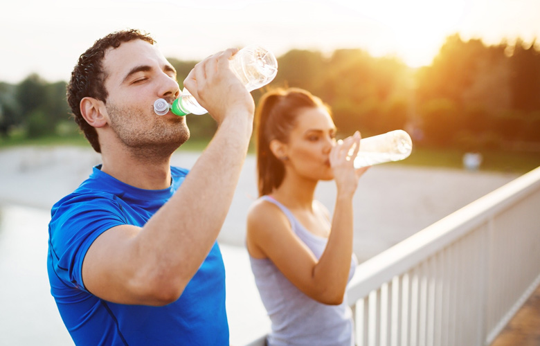 Hombre y mujer adultos en un puente bebiendo agua con ropa para hacer ejercicio.